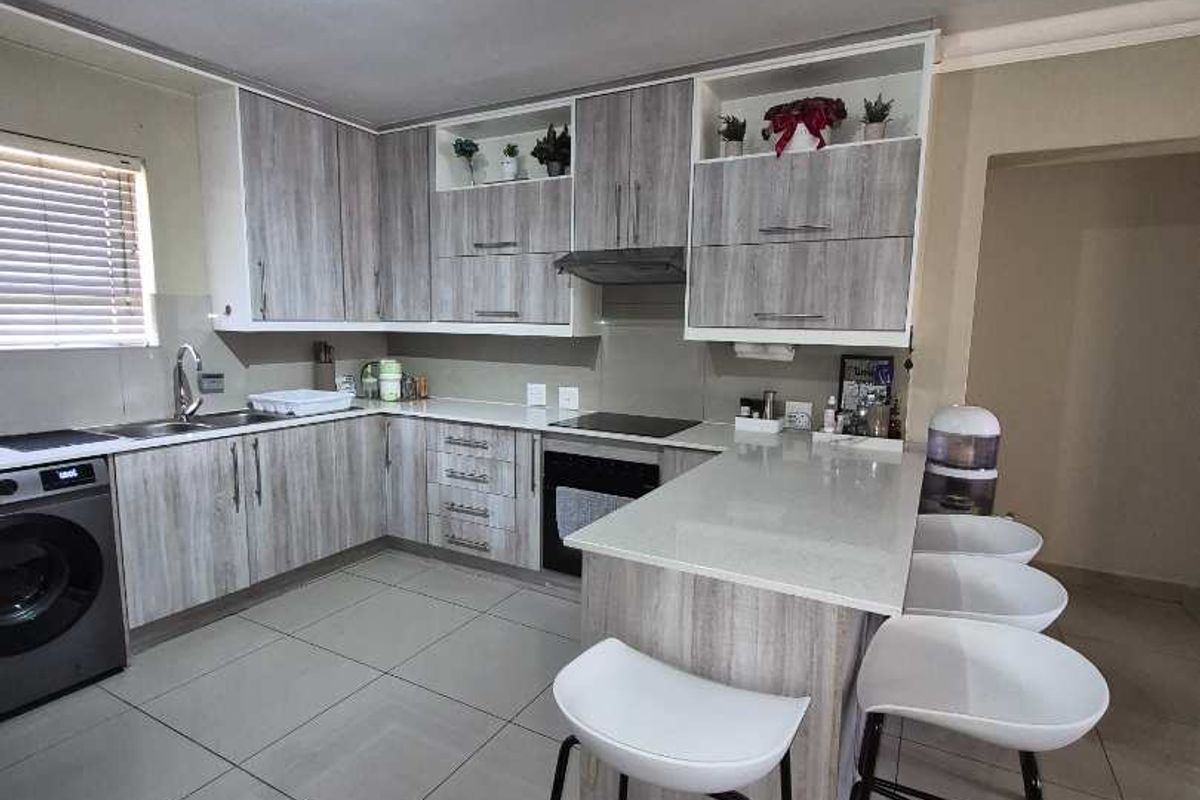 Modern kitchen featuring light wood-grain cabinetry, stone countertops, a breakfast bar, and integrated appliances with sleek tiled flooring.