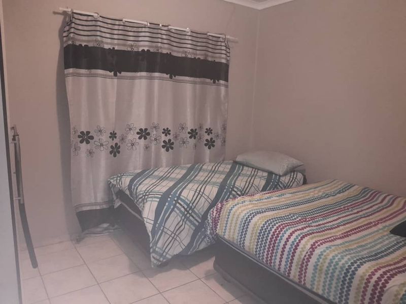 A bedroom featuring tiled flooring and a curtain rod, providing a functional space for sleeping arrangements.