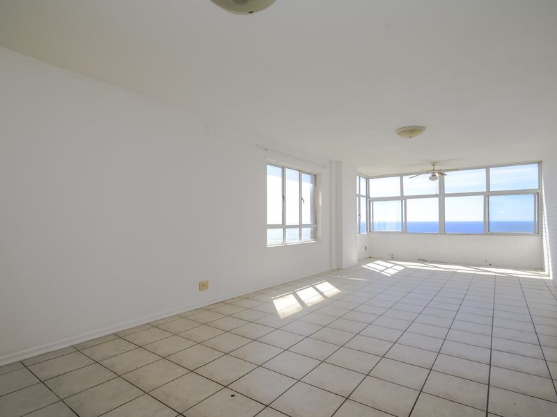 Spacious, empty living area featuring tiled flooring, a ceiling fan, and expansive windows offering direct ocean views.