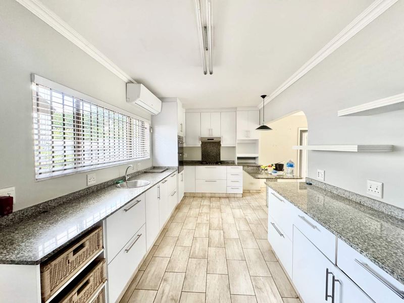 A bright, modern kitchen featuring granite countertops, ample white cabinetry, built-in appliances, and tiled flooring, offering a clean and functional workspace.