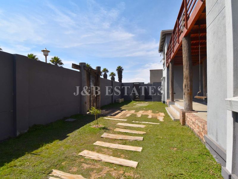 A rear garden area featuring a covered patio with timber support posts, a paved walkway, and a high perimeter boundary wall.