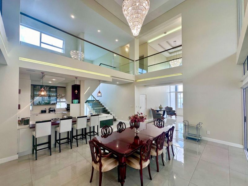 Spacious open-plan living and dining area featuring a modern kitchen with island, double-volume ceilings, glass balustrades, and high-end finishes throughout.