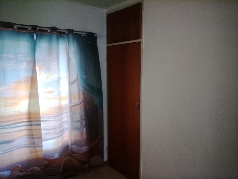 A bedroom interior featuring a built-in wooden cupboard and a window with a curtain.