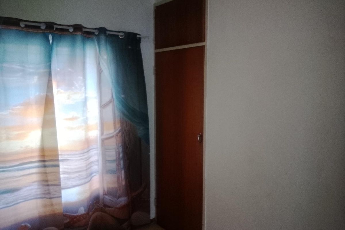A bedroom interior featuring a built-in wooden cupboard and a window with a curtain.