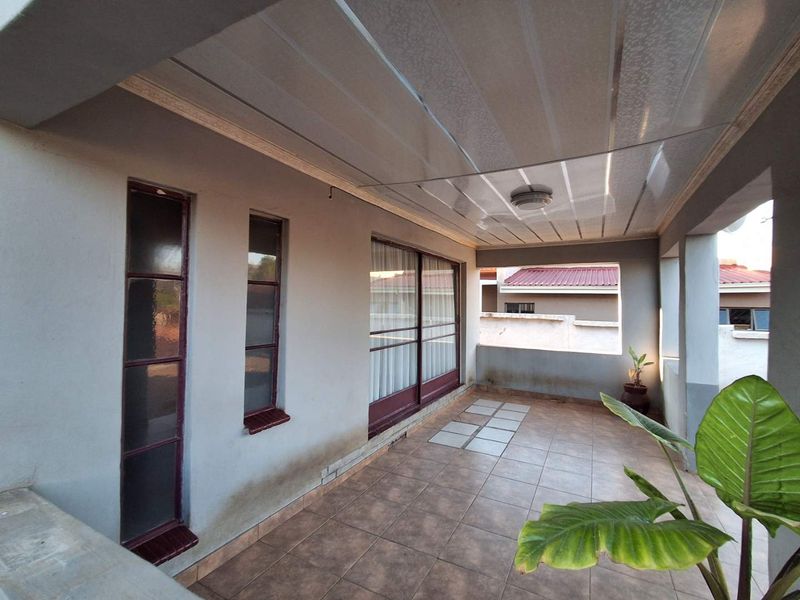 A covered patio area featuring tiled flooring, sliding glass doors, and ceiling panels, offering a functional outdoor space for relaxation.