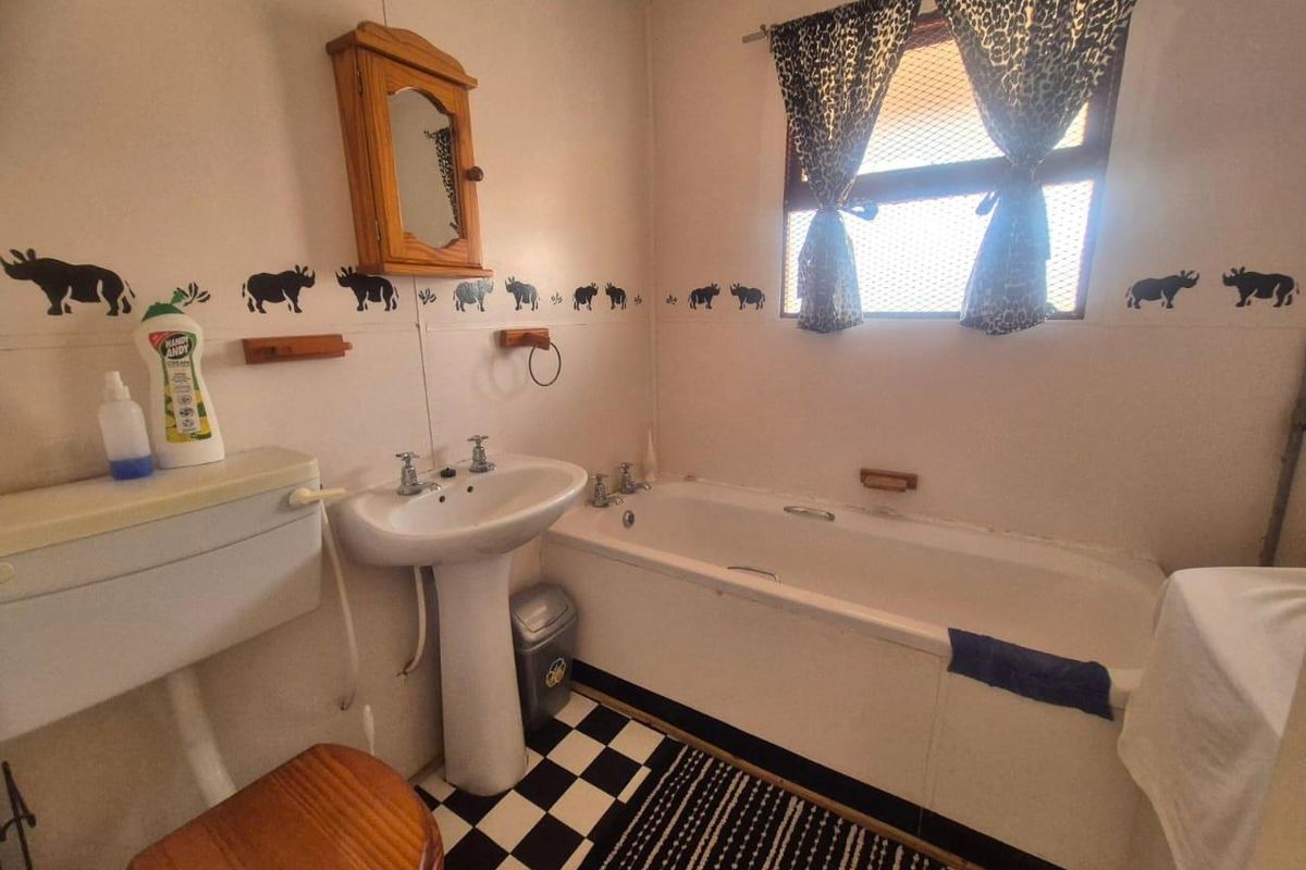 A dated bathroom featuring a standard pedestal basin, bathtub, and toilet, with a classic checkerboard floor and wall-mounted storage cabinet.
