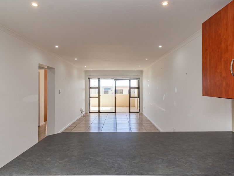 An open-plan living area featuring tiled floors, recessed lighting, and direct access to a balcony through sliding glass doors.