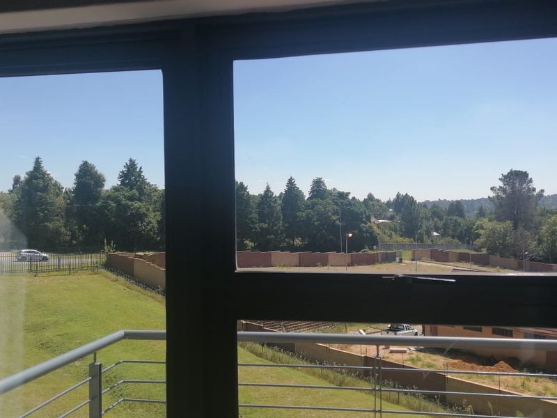 A view from an apartment window overlooking a green landscape, trees, and a residential area with a metal balcony railing visible.