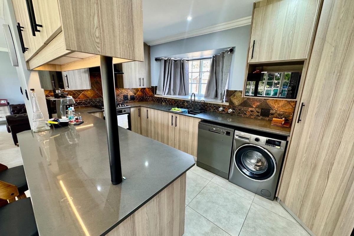 Modern kitchen featuring light wood cabinetry, dark stone countertops, tiled backsplash, and integrated space for laundry appliances.