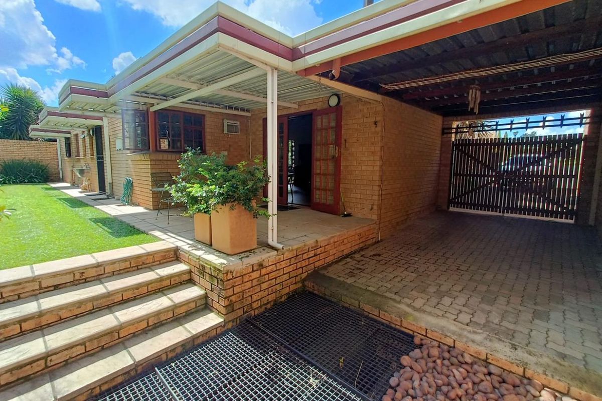 Rear exterior view featuring a covered patio, brick facade, paved driveway area, and a well-maintained lawn with stepped access.