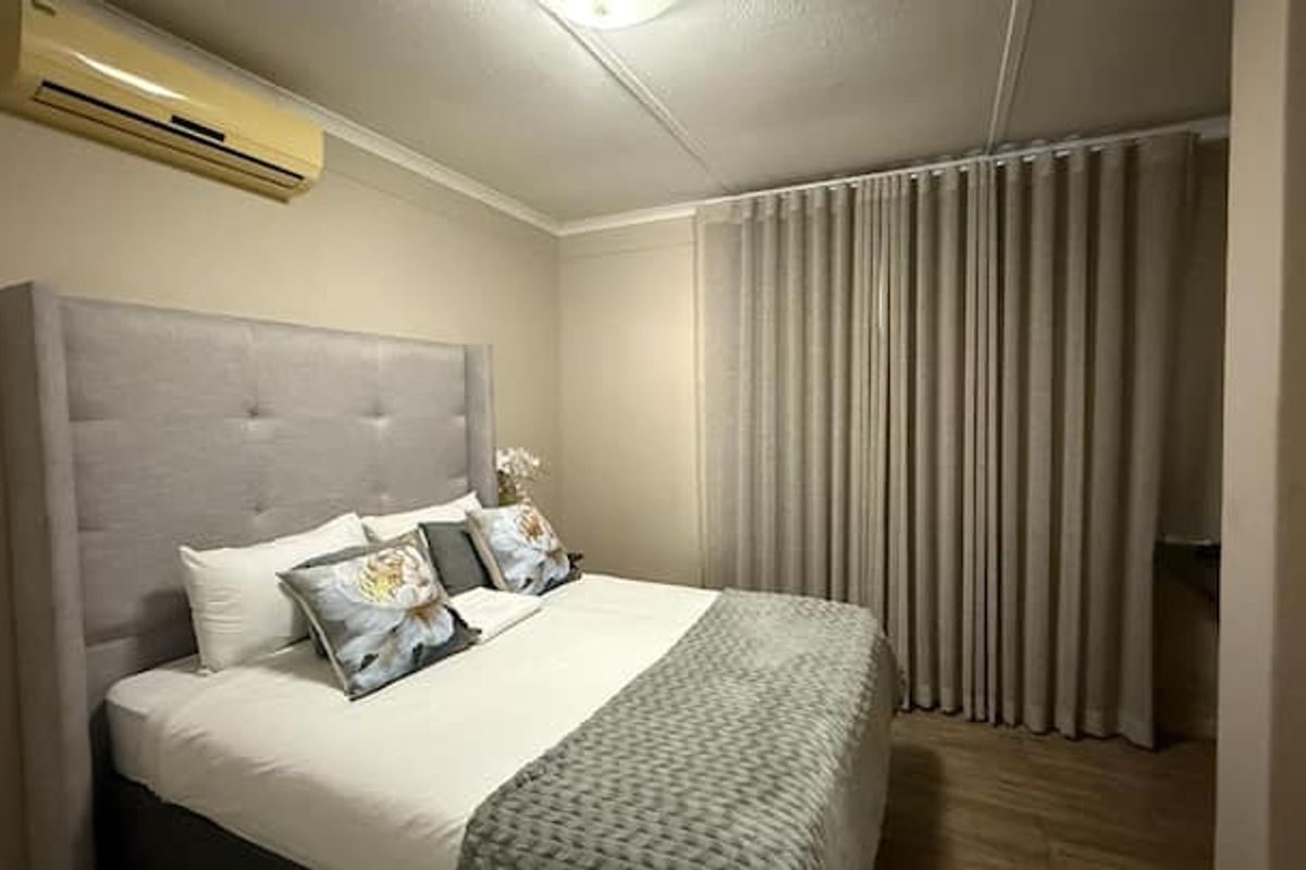 A bedroom featuring laminate flooring, full-length curtains, and a wall-mounted split-system air conditioning unit.