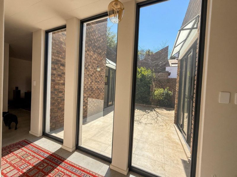 Bright living area featuring floor-to-ceiling windows, exposed brick walls, and tiled flooring, offering a seamless transition to the outdoor patio space.