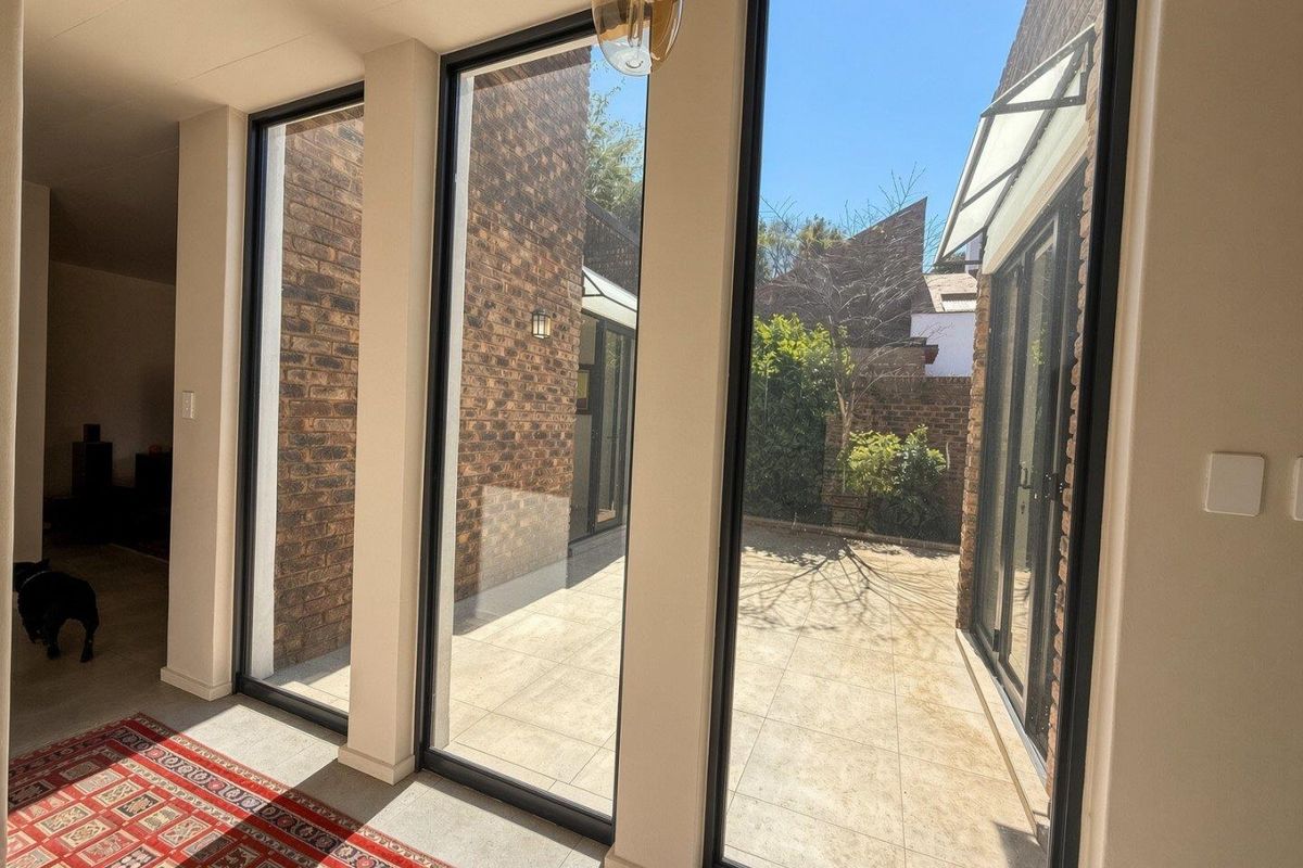 Bright living area featuring floor-to-ceiling windows, exposed brick walls, and tiled flooring, offering a seamless transition to the outdoor patio space.