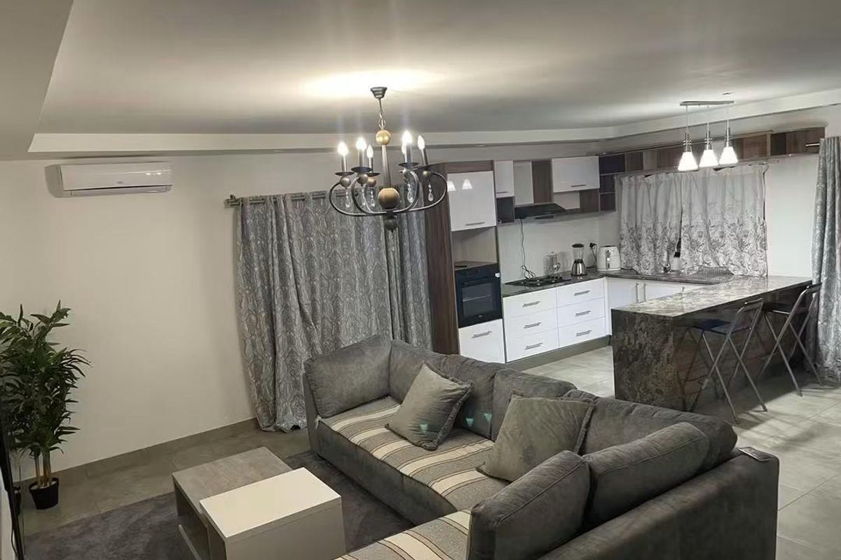 Modern open-plan living area featuring a well-appointed kitchen with stone-look island, built-in appliances, and neutral tiled flooring throughout.