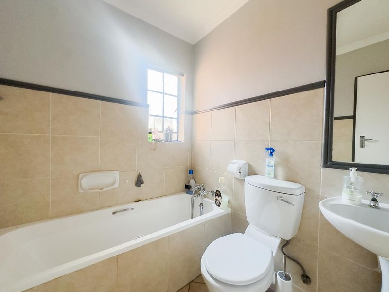 A functional bathroom featuring a bathtub, toilet, and pedestal basin with neutral wall tiling and a framed mirror.