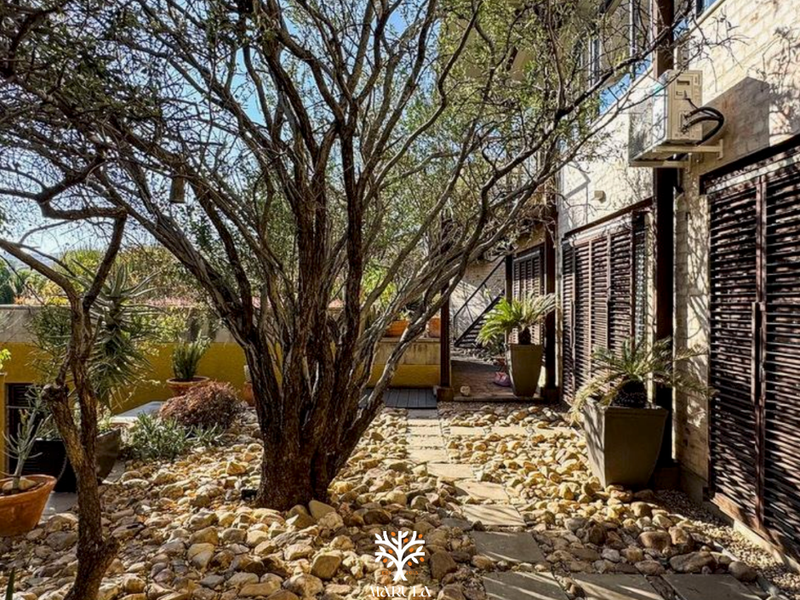A landscaped rear garden area featuring stone ground cover, a paved pathway, and exterior wall-mounted air conditioning unit with timber shutters.