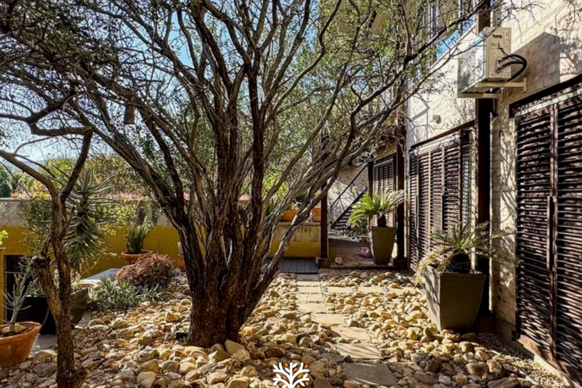 A landscaped rear garden area featuring stone ground cover, a paved pathway, and exterior wall-mounted air conditioning unit with timber shutters.