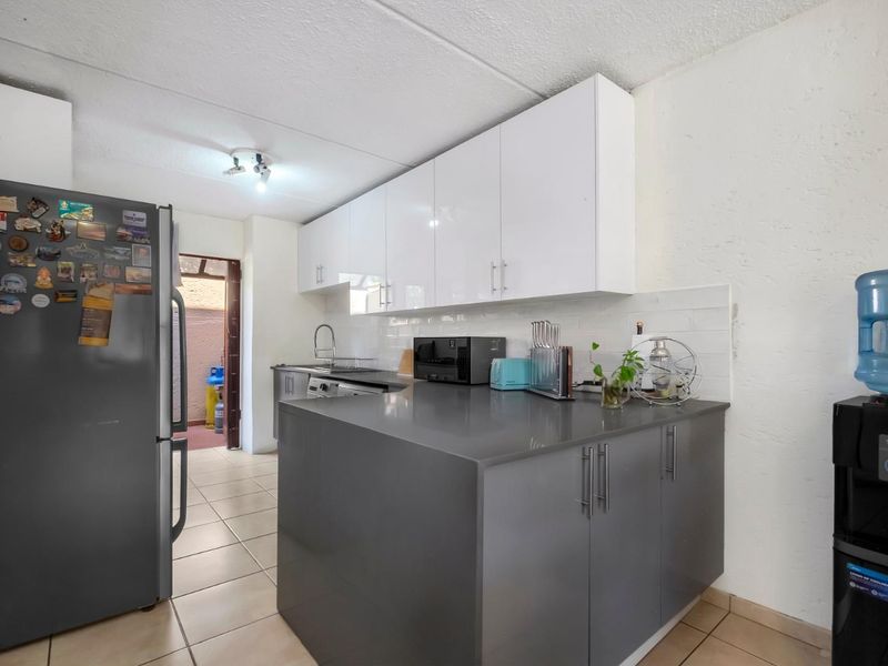 A functional kitchen featuring modern grey lower cabinets, white upper cabinetry, stone countertops, and a subway tile backsplash with tiled flooring.