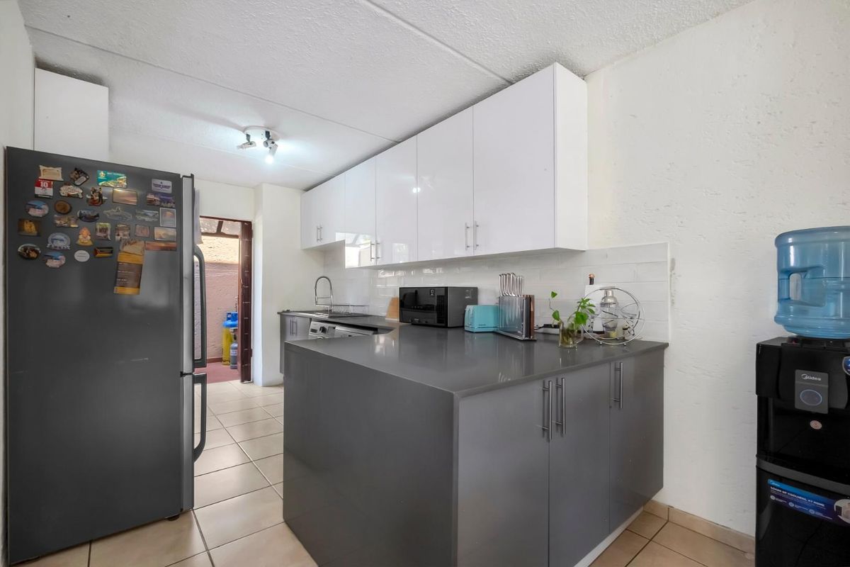 A functional kitchen featuring modern grey lower cabinets, white upper cabinetry, stone countertops, and a subway tile backsplash with tiled flooring.