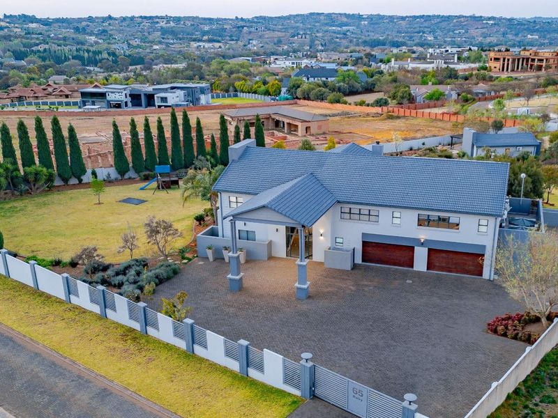Aerial view of a modern residential property featuring a tiled roof, double garage, paved driveway, and secure perimeter walling in a suburban estate setting.