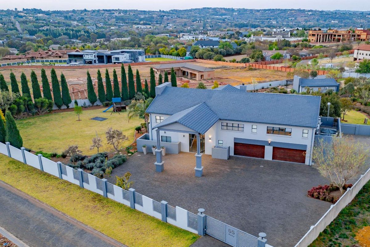 Aerial view of a modern residential property featuring a tiled roof, double garage, paved driveway, and secure perimeter walling in a suburban estate setting.