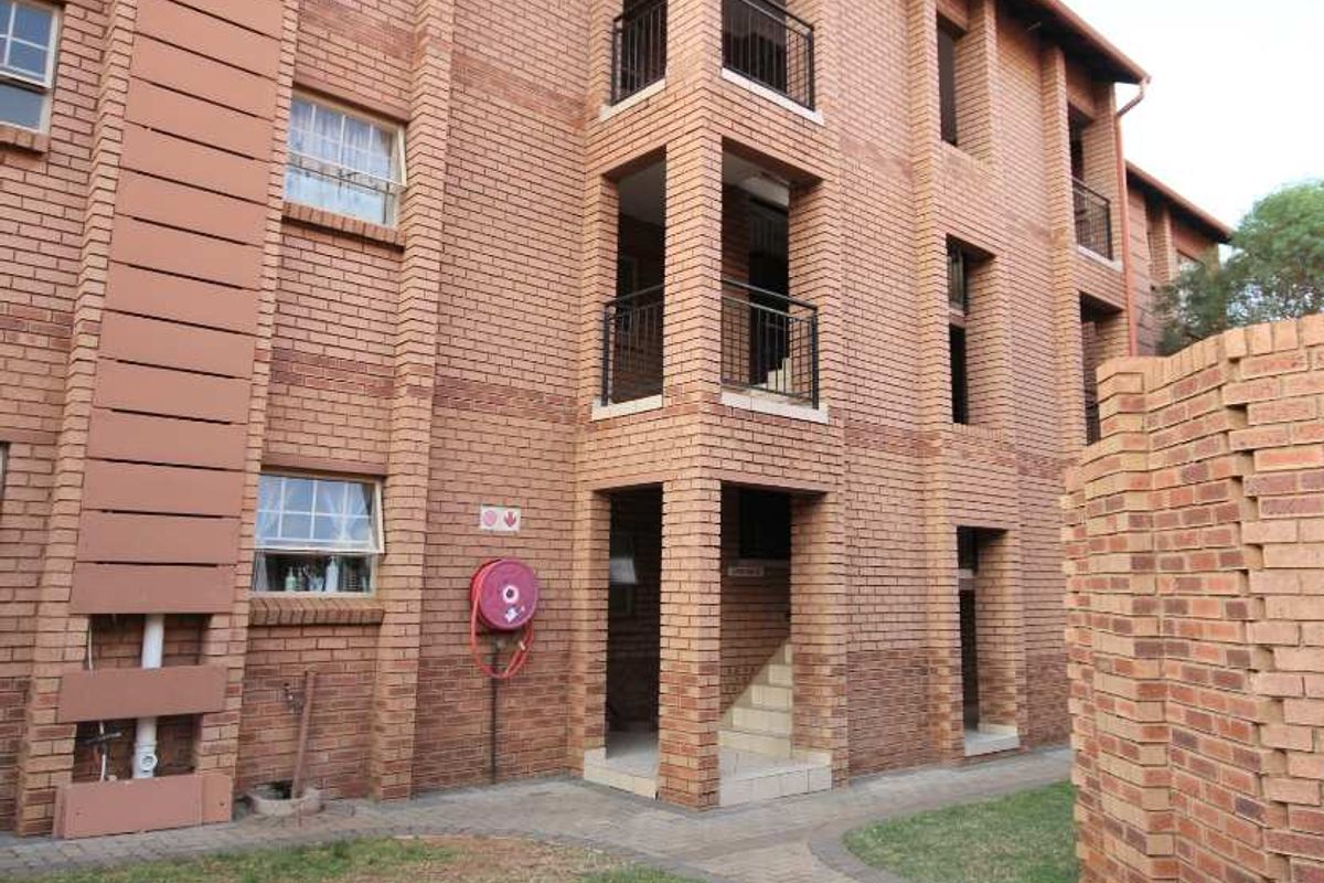 Exterior view of a multi-story face brick apartment building featuring private balconies, paved walkways, and established garden areas.