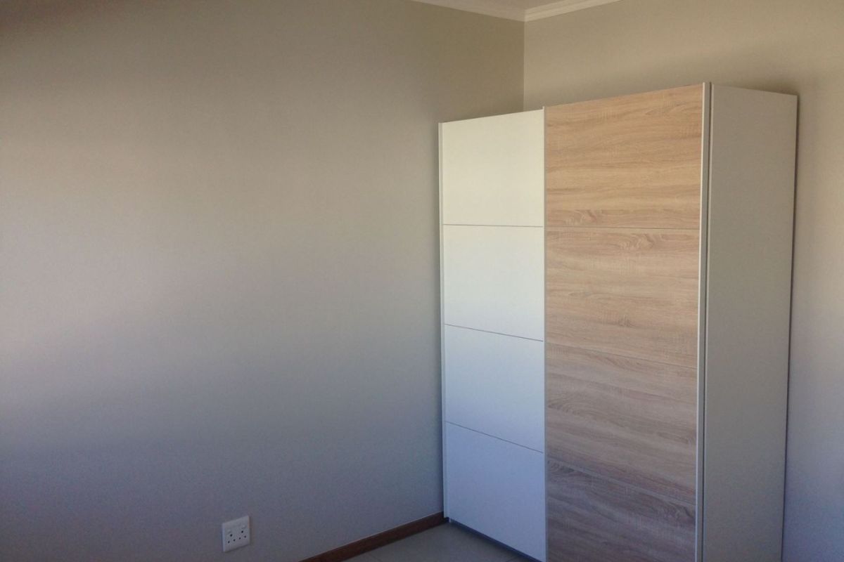A bedroom featuring a modern built-in wardrobe with a two-tone white and wood-grain finish, set against neutral walls and tiled flooring.
