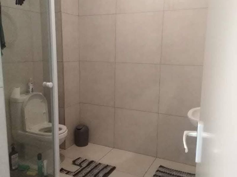 A functional bathroom featuring floor-to-ceiling wall tiles, a glass shower enclosure, a standard toilet, and a wall-mounted washbasin.