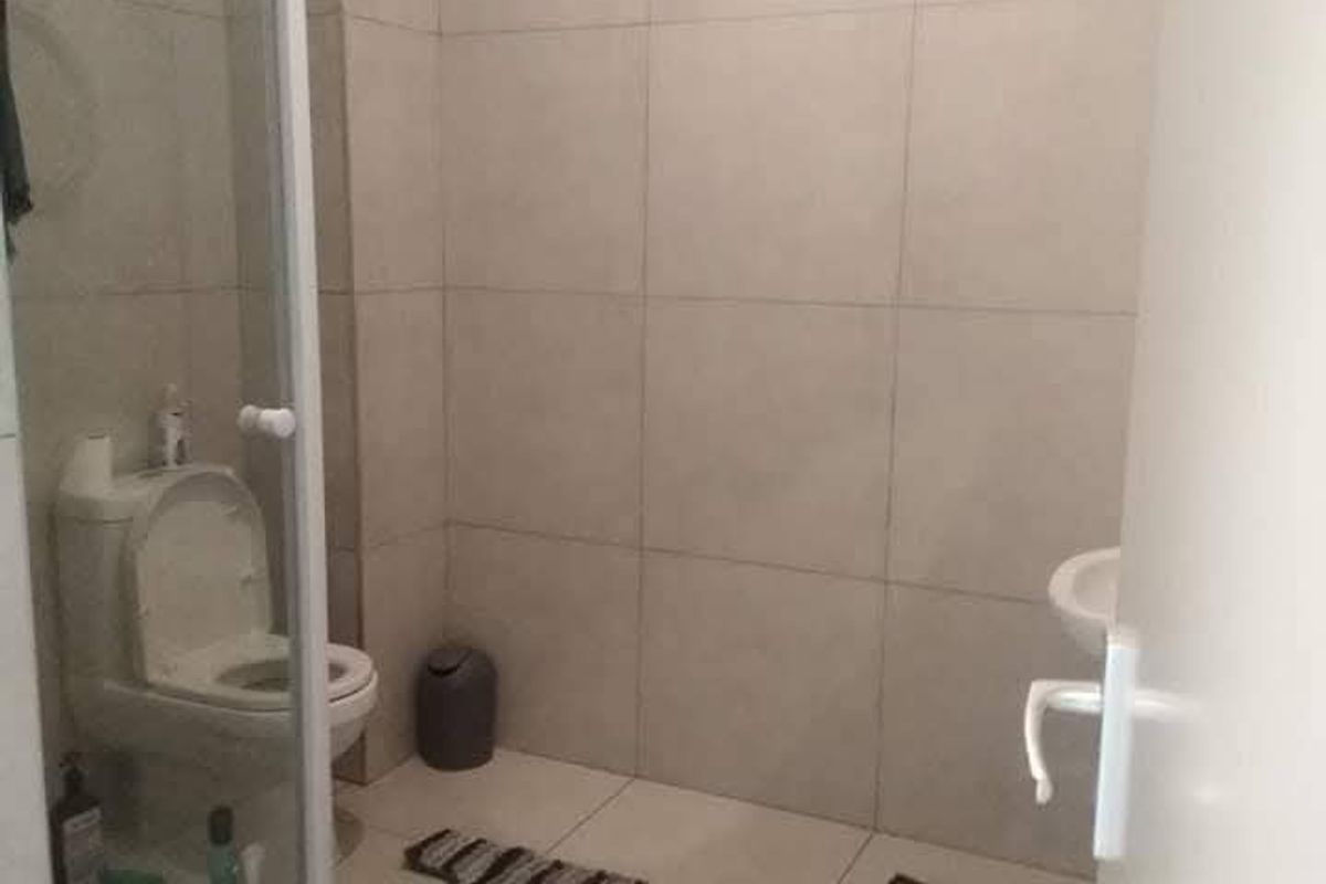 A functional bathroom featuring floor-to-ceiling wall tiles, a glass shower enclosure, a standard toilet, and a wall-mounted washbasin.