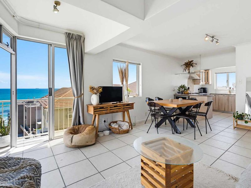 Bright open-plan living and dining area featuring tiled floors, a modern kitchen, and direct access to a balcony with scenic ocean views.