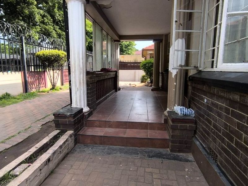 A covered outdoor patio area featuring tiled flooring, brick pillars, and decorative columns, requiring some maintenance to the ceiling and paintwork.