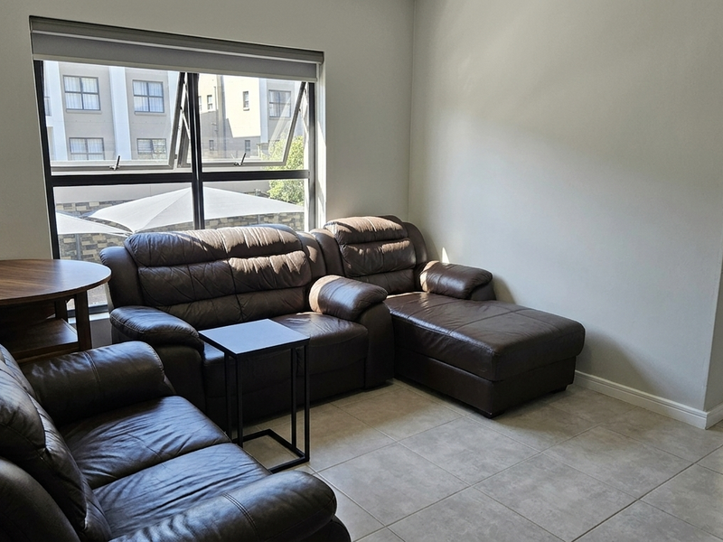 A bright living room featuring neutral tiled flooring, large aluminium-framed windows with roller blinds, and a clean, minimalist aesthetic.