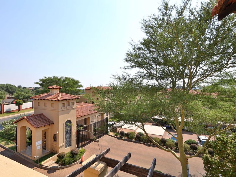 Elevated view overlooking the complex entrance, paved driveway, security gatehouse, and surrounding landscaped grounds.