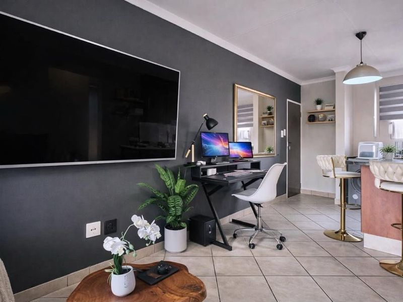 Modern open-plan living area featuring tiled flooring, a dark accent wall, and a functional kitchen breakfast bar with integrated lighting.