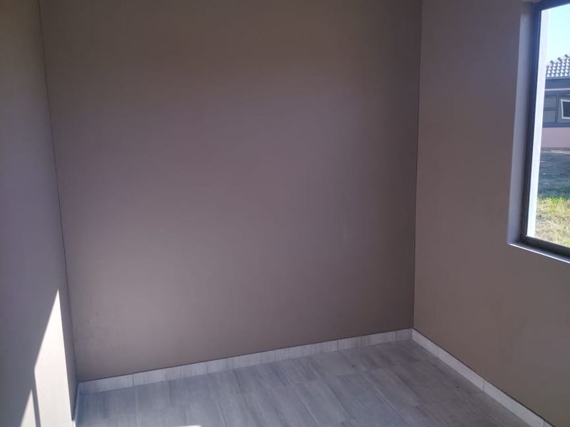 A clean, empty bedroom featuring neutral-toned walls and light-colored wood-look floor tiles, providing a versatile space ready for furnishing.