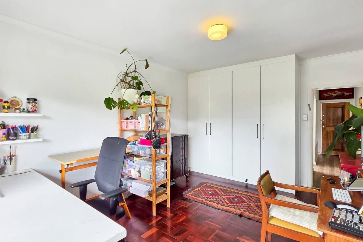 A bedroom featuring classic parquet flooring and ample built-in cupboard storage, currently utilized as a home office space.