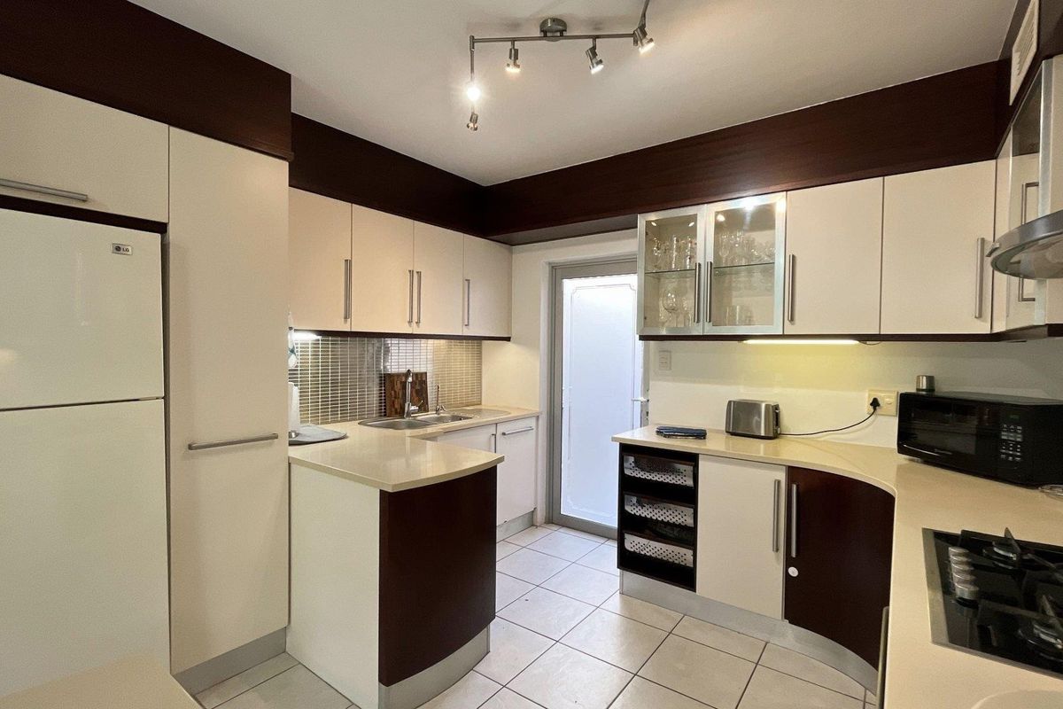 A well-maintained kitchen featuring two-tone cabinetry, stone countertops, mosaic tile backsplash, and integrated gas cooktop with extractor fan.