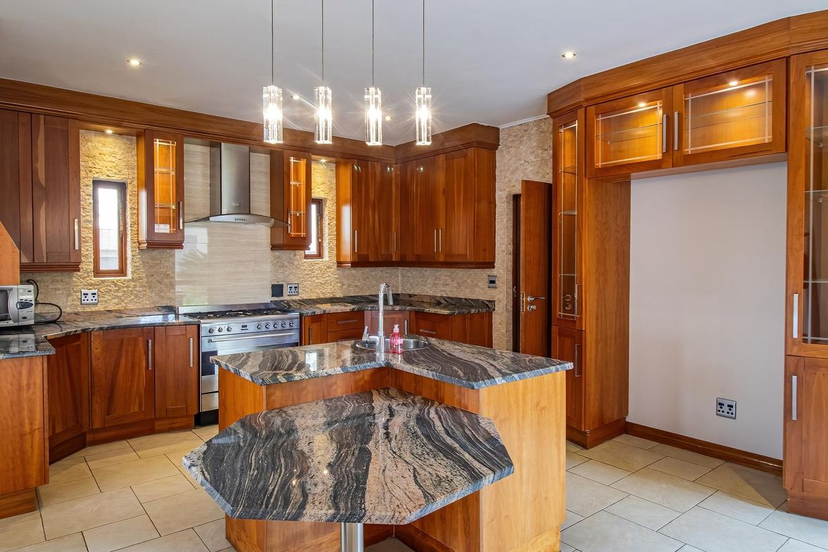Spacious kitchen featuring rich wooden cabinetry, granite countertops, a central island with breakfast bar, and stainless steel appliances including a gas range and extractor.