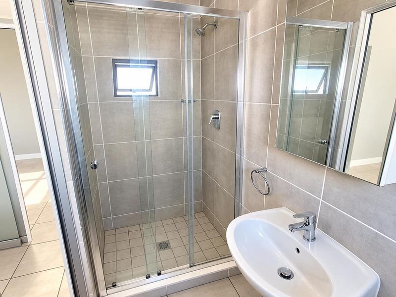 A clean, modern bathroom featuring a glass-enclosed shower, pedestal basin, and neutral wall tiling.