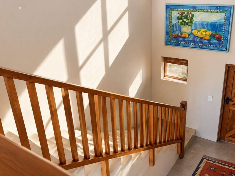 A bright hallway featuring a wooden staircase with a matching balustrade, a solid timber door, and natural light casting geometric shadows on the wall.