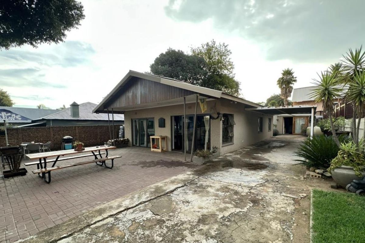 Rear exterior view of the house featuring a paved patio area, covered walkway, and a large, weathered concrete driveway.