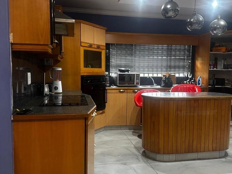 A functional kitchen featuring wooden cabinetry, granite countertops, a central island, and tiled flooring, illuminated by recessed and pendant lighting.