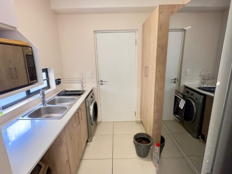 A functional laundry room featuring built-in cabinetry, a double stainless steel sink, stone countertops, and space for a washing machine.