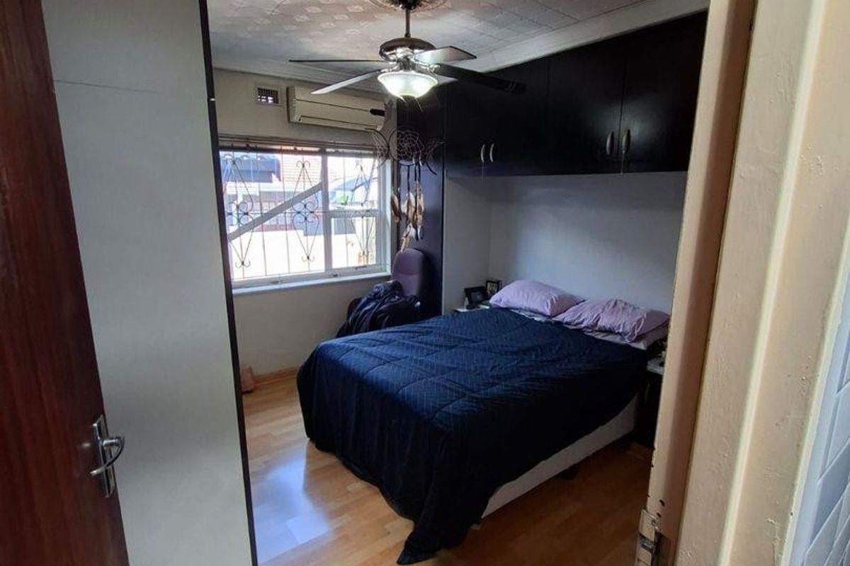 A bedroom featuring built-in overhead cabinetry, a ceiling fan, and a wall-mounted air conditioning unit.