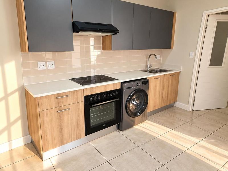 Modern kitchen featuring sleek grey and wood-grain cabinetry, integrated electric hob, oven, extractor fan, and tiled flooring in a clean, well-lit space.