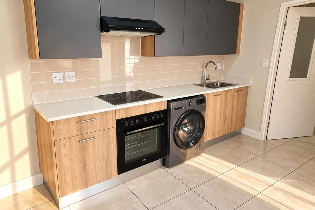 Modern kitchen featuring sleek grey and wood-grain cabinetry, integrated electric hob, oven, extractor fan, and tiled flooring in a clean, well-lit space.
