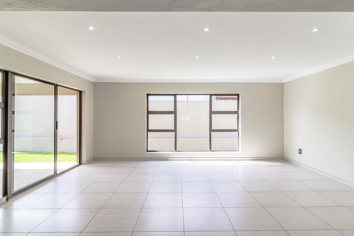 A bright, spacious, and empty living area featuring neutral tiled flooring, recessed ceiling lighting, and large sliding glass doors leading to the exterior.