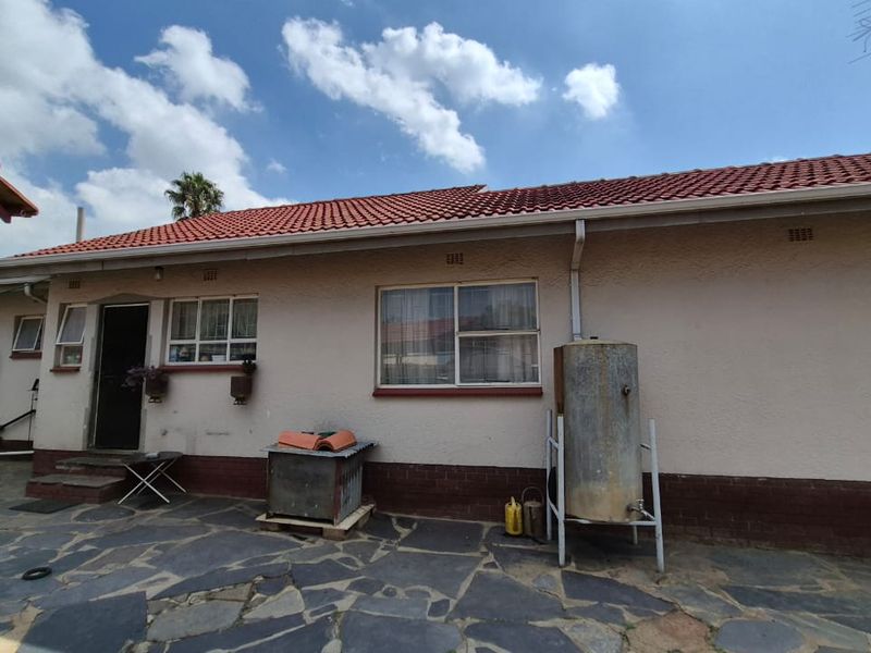 Rear exterior view of the house featuring a tiled roof, stone paved patio area, and an external water tank.