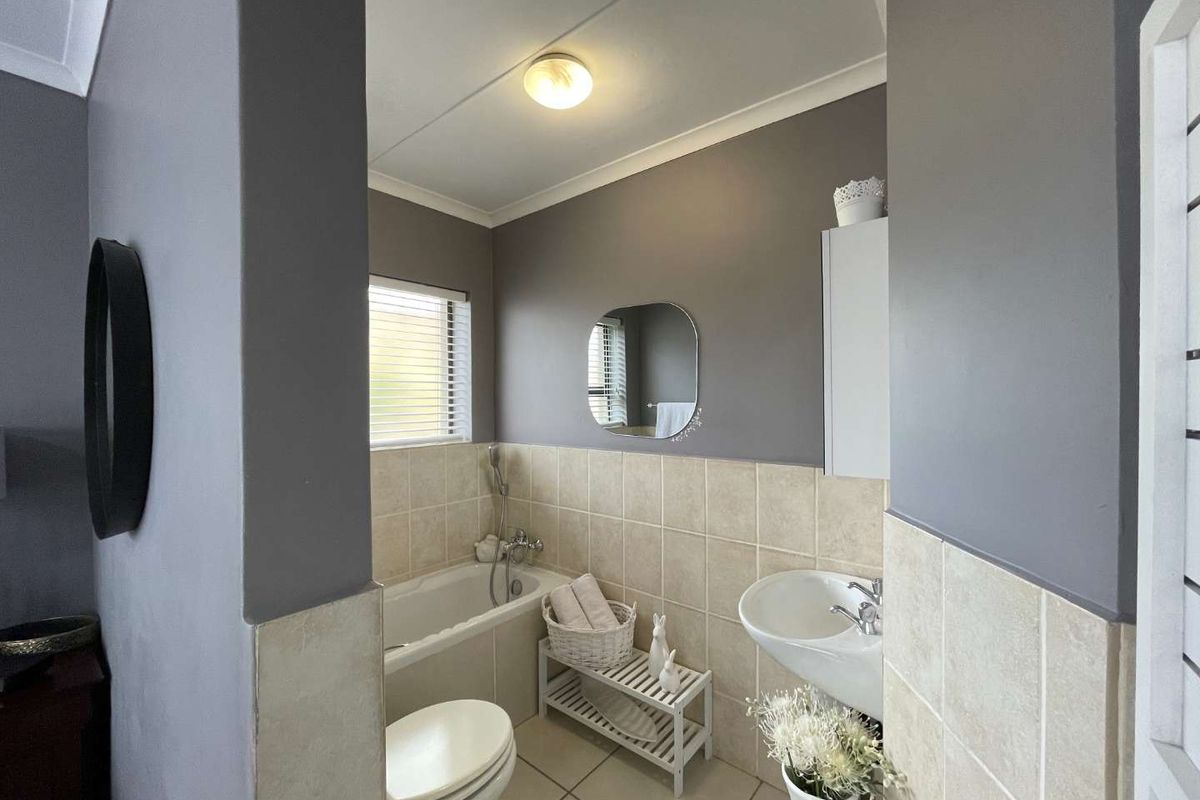 A compact bathroom featuring a built-in bathtub with shower mixer, a pedestal basin, and tiled wall finishes.