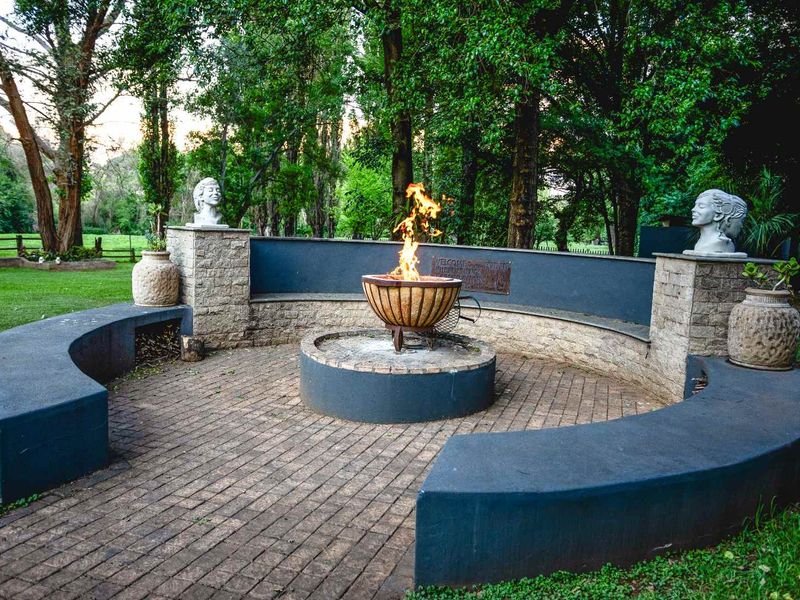 A landscaped garden area featuring a circular brick-paved fire pit with built-in curved seating and stone masonry accents.